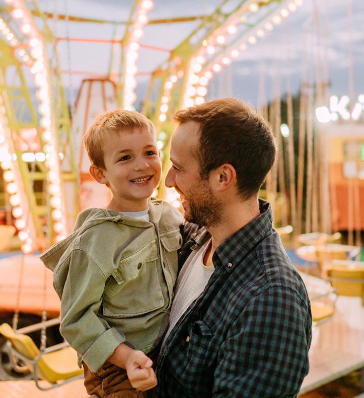 Child being held by parent in front of merry-go-round